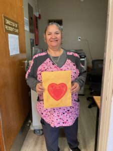 Picture of woman smiling holding yellow Valentine's Day card with a red heart in the middle.